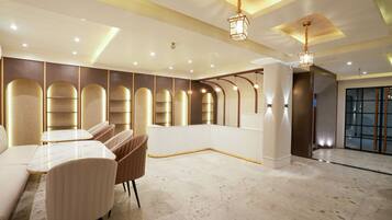 A modern hotel lobby with a marble floor, seating area with tables and chairs, and a large glass door entrance.
