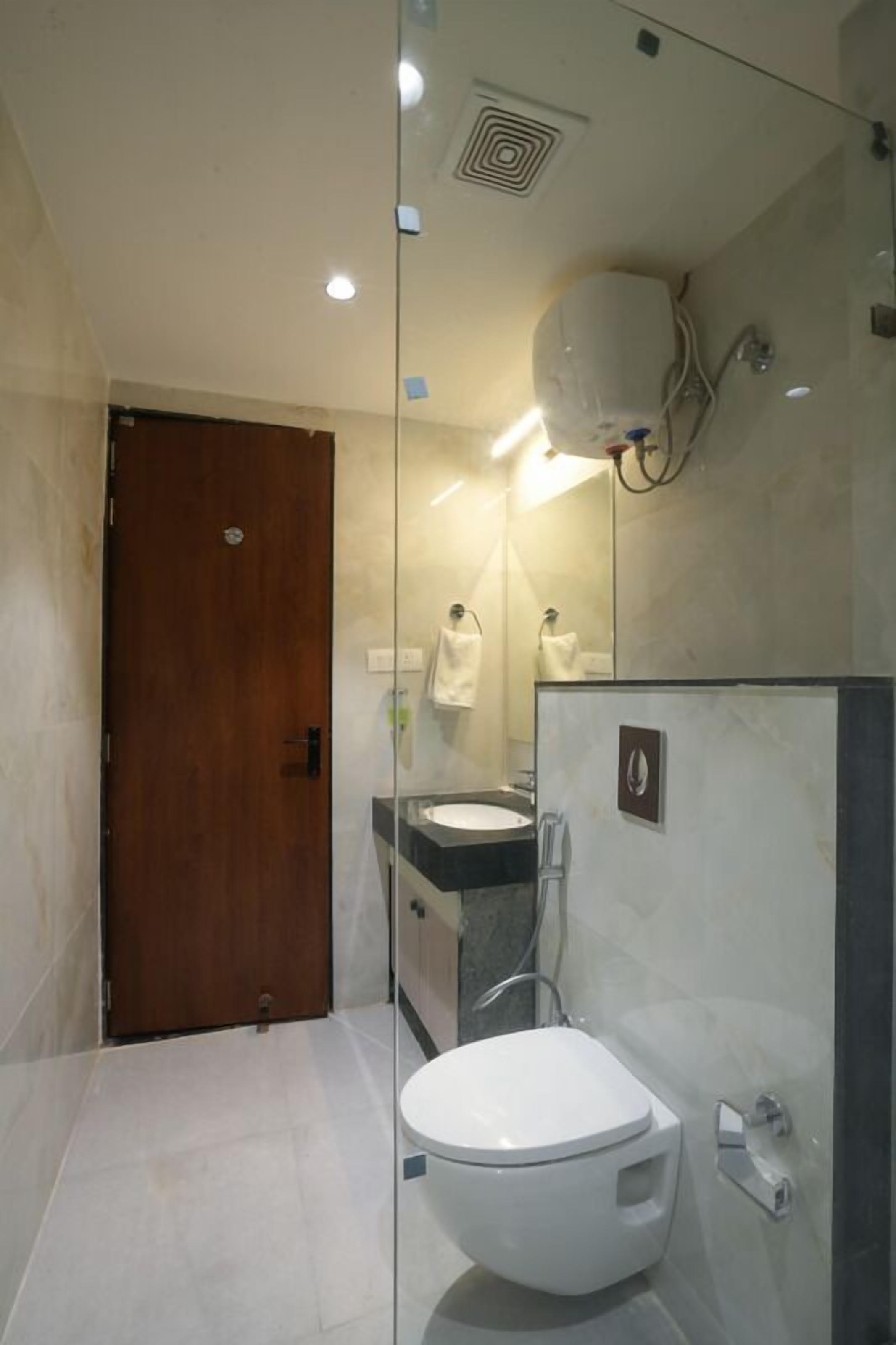 Een moderne badkamer met een glazen douchewand, een houten deur, een wit toilet, een wastafel en een handdoekhouder.