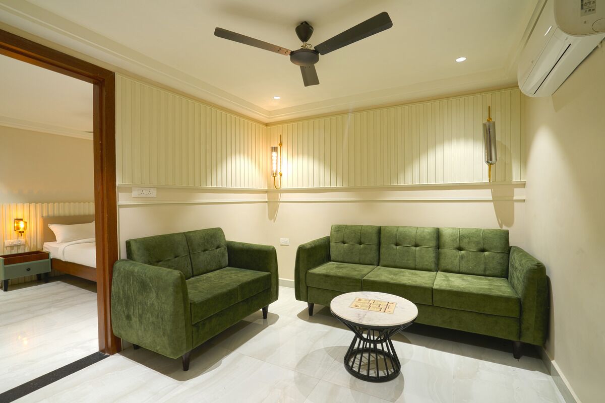 Ein Hotelzimmer mit zwei grünen Sofas, einem runden Couchtisch, einem Deckenventilator und einem Bett im Hintergrund.