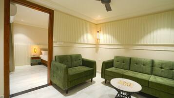 A room with two green sofas, a small round table, a ceiling fan, and a nightstand with a lamp.