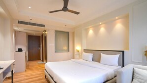 A hotel room with a large bed, a desk, a chair, and a ceiling fan. - Hotel Square 36 (Kota)
