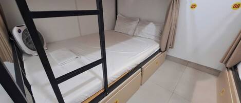 A bunk bed with a fan, a small cabinet, and a curtain.