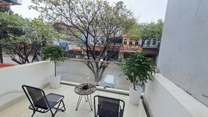 A balcony with two chairs and a small table, overlooking a street with buildings and trees. - HT Airport Inn (Hanoi)