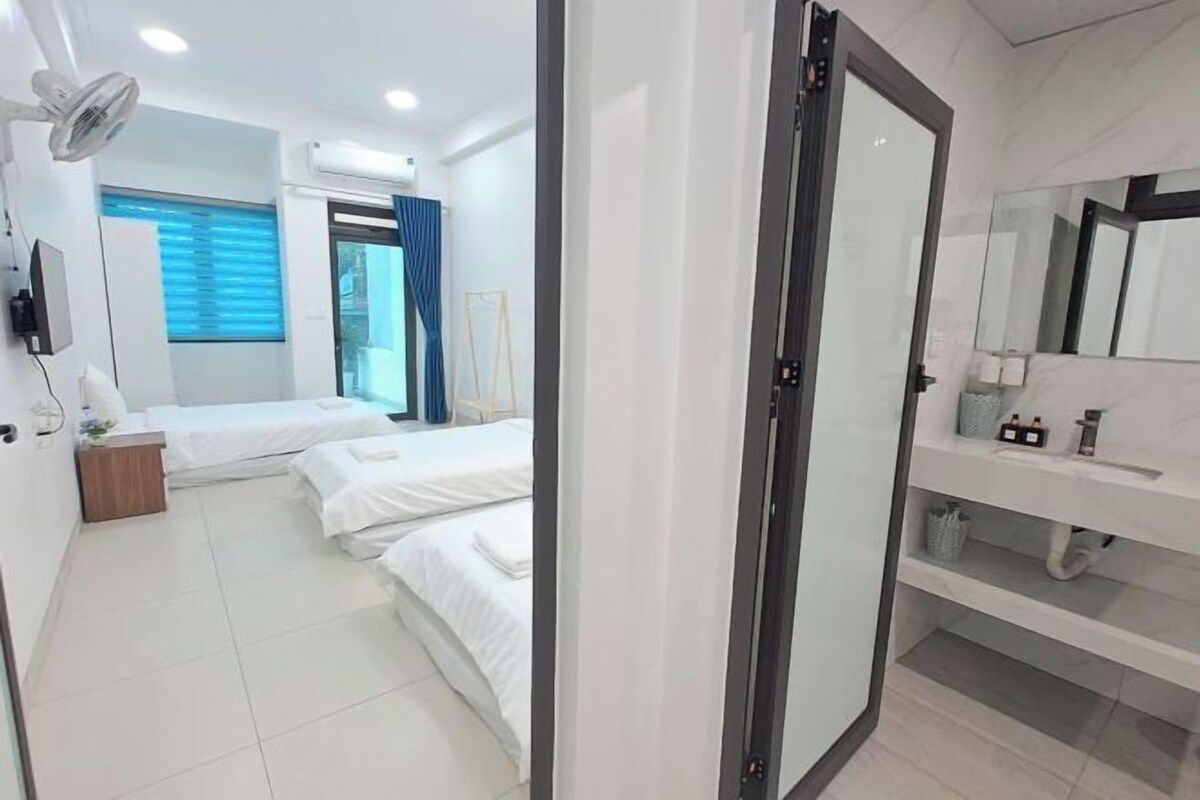 A hotel room with two beds, a large mirror, a bedside table, and a bathroom with a sink and mirror.