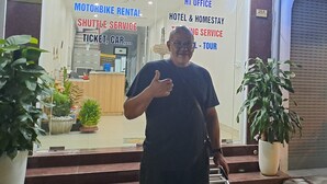 A man standing in front of a building with signs for motorbike rental, shuttle service, hotel & homestay, and tour services. - HT Airport Inn (Hanoi)