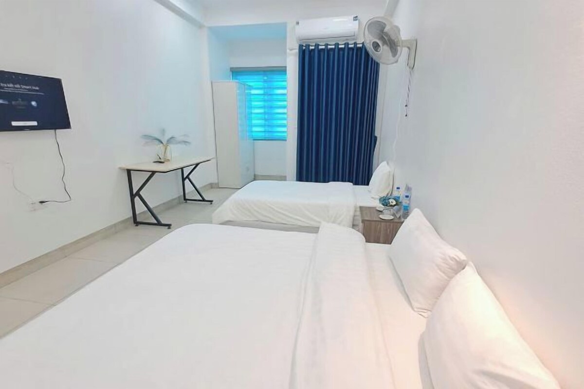 A hotel room with two beds, a small table, a TV, and a window with curtains.