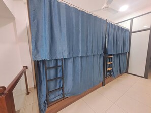 A room with a wooden floor, a staircase, a ceiling fan, and a window with blue curtains. - HT Airport Inn (Hanoi)
