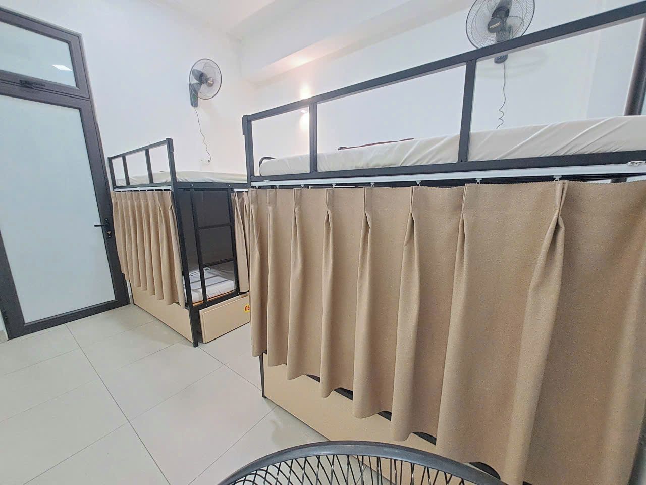 A dormitory room with bunk beds, a fan, and a curtain.