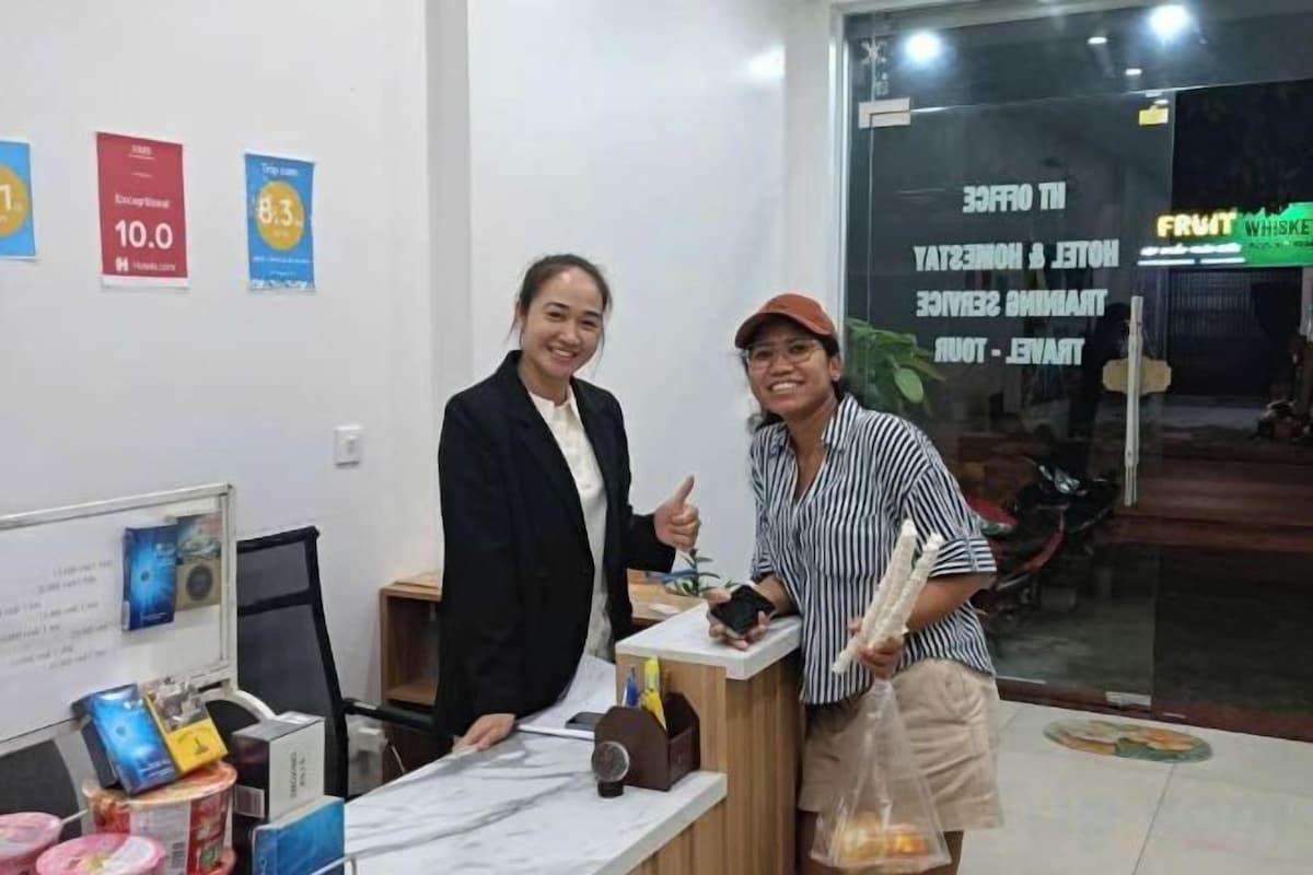 Two individuals standing in a reception area with a counter, a computer, and a glass door leading outside.