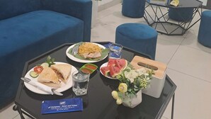 A hotel reception area with a blue sofa, a small table with a meal, a flower vase, and a poster advertising tours. - HT Airport Inn (Hanoi)