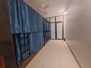 A hallway with blue curtains, a ceiling fan, and a tiled floor. - HT Airport Inn (Hanoi)