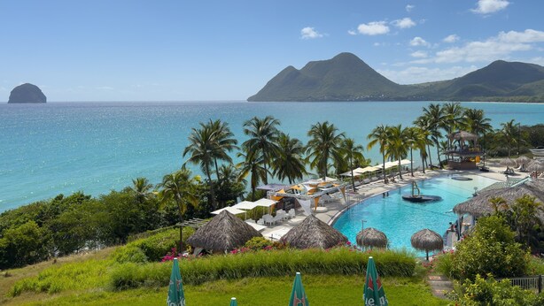Un resort con piscina, palmeras y montañas al fondo.