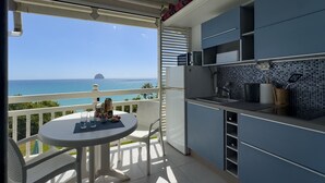 Un balcón con vista al mar y una pequeña isla. Se observa una mesa redonda con sillas y un refrigerador.