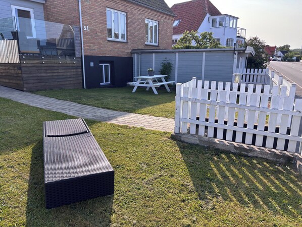 Un quartier résidentiel avec un chemin pavé, une clôture blanche en bois et un banc en osier.