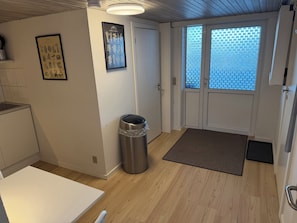 A compact kitchen with a trash bin, a framed vegetable garden poster, and a door with frosted glass panels.