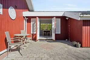 A red building with a patio area featuring a table and chairs, a door, and potted plants.