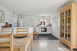 A modern kitchen with white cabinetry, a dining area with wooden furniture, and a wooden cabinet with glass doors.