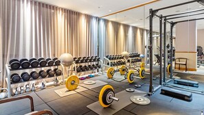 Un gimnasio con equipo de levantamiento de pesas, mancuernas y colchonetas de ejercicio.