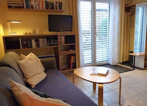 Una sala de estar con un sofá, televisor, estantería, una mesita y un ventanal corredero.