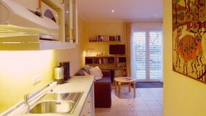 A kitchen with a sink, a dining area with a table and chairs, a bookshelf, and a large window with blinds.
