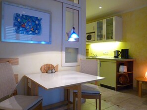 Une cuisine compacte avec un coin repas, une œuvre d’art encadrée au mur et une petite table avec des chaises.