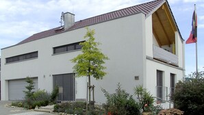 A modern two-story building with a sloped roof, a satellite dish, and a flagpole.