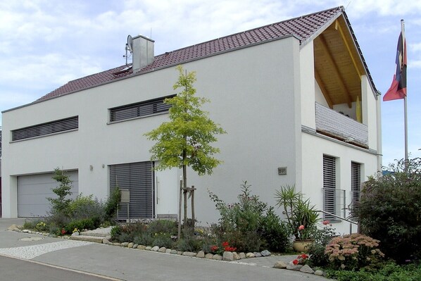 Un bâtiment moderne à deux étages, doté d’un toit en pente, d’une antenne parabolique et d’un mât pour drapeau.