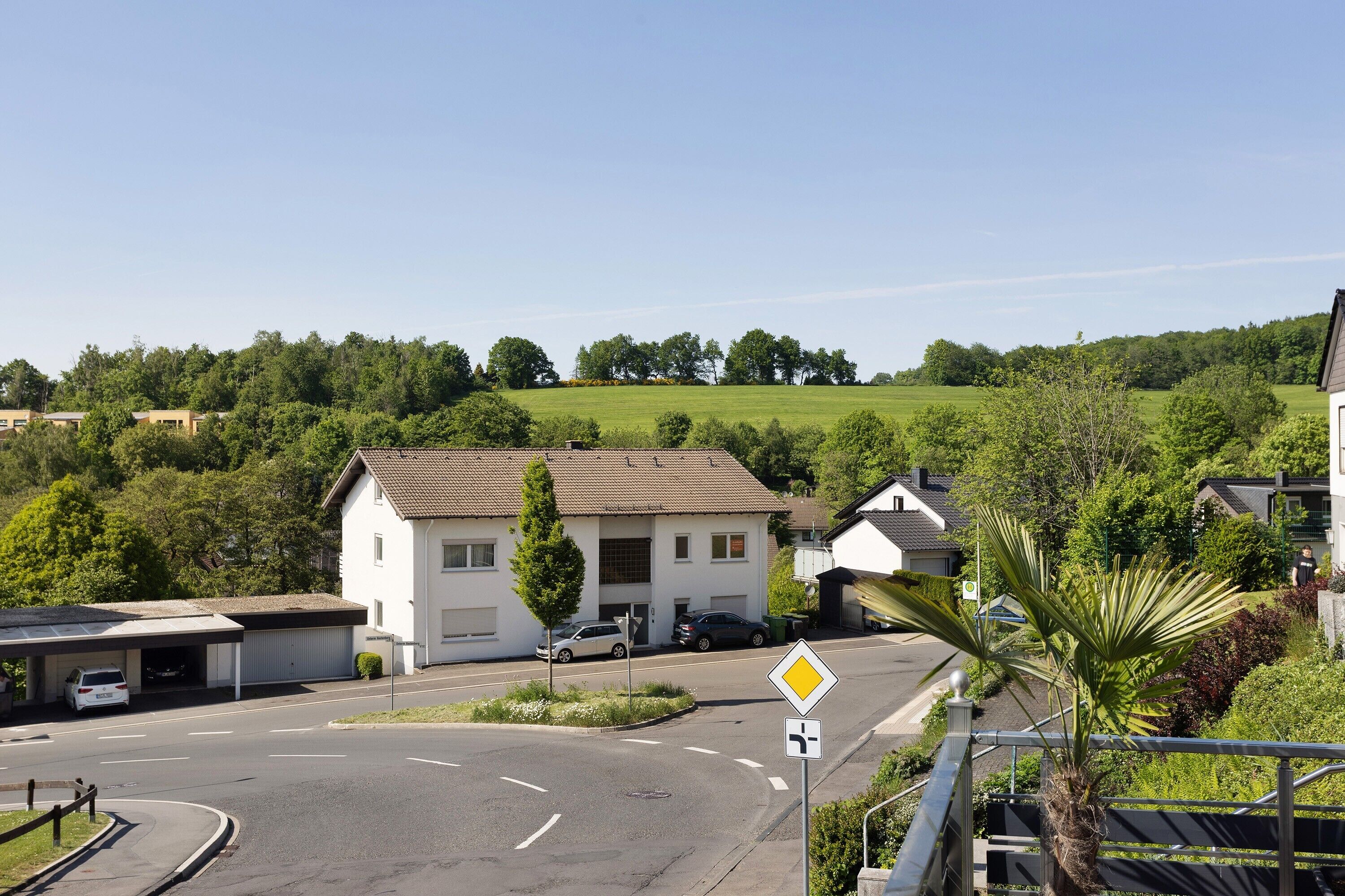 A residential area with a white house, a roundabout, and a clear sky.