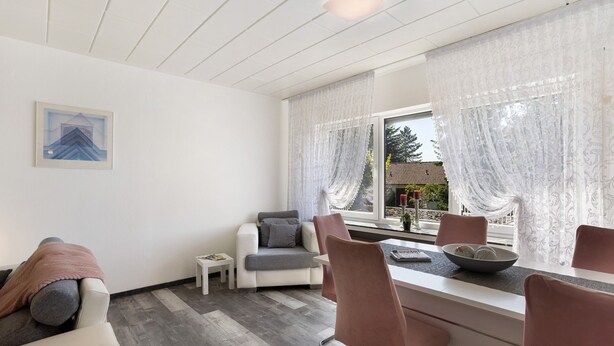 Una sala de estar moderna con un sofá, una mesa de comedor con sillas, una mesita auxiliar y una ventana con cortinas.
