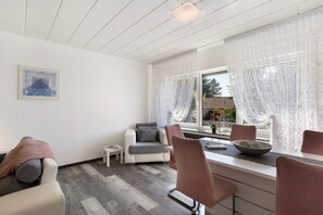Een moderne woonkamer met een bank, een eettafel met stoelen, een klein bijzettafeltje en een raam met gordijnen.