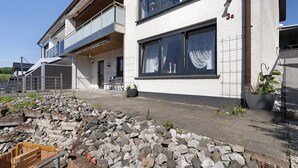 Un edificio moderno de dos pisos, con balcón, ventanas amplias y un camino de piedra que lleva a la entrada.
