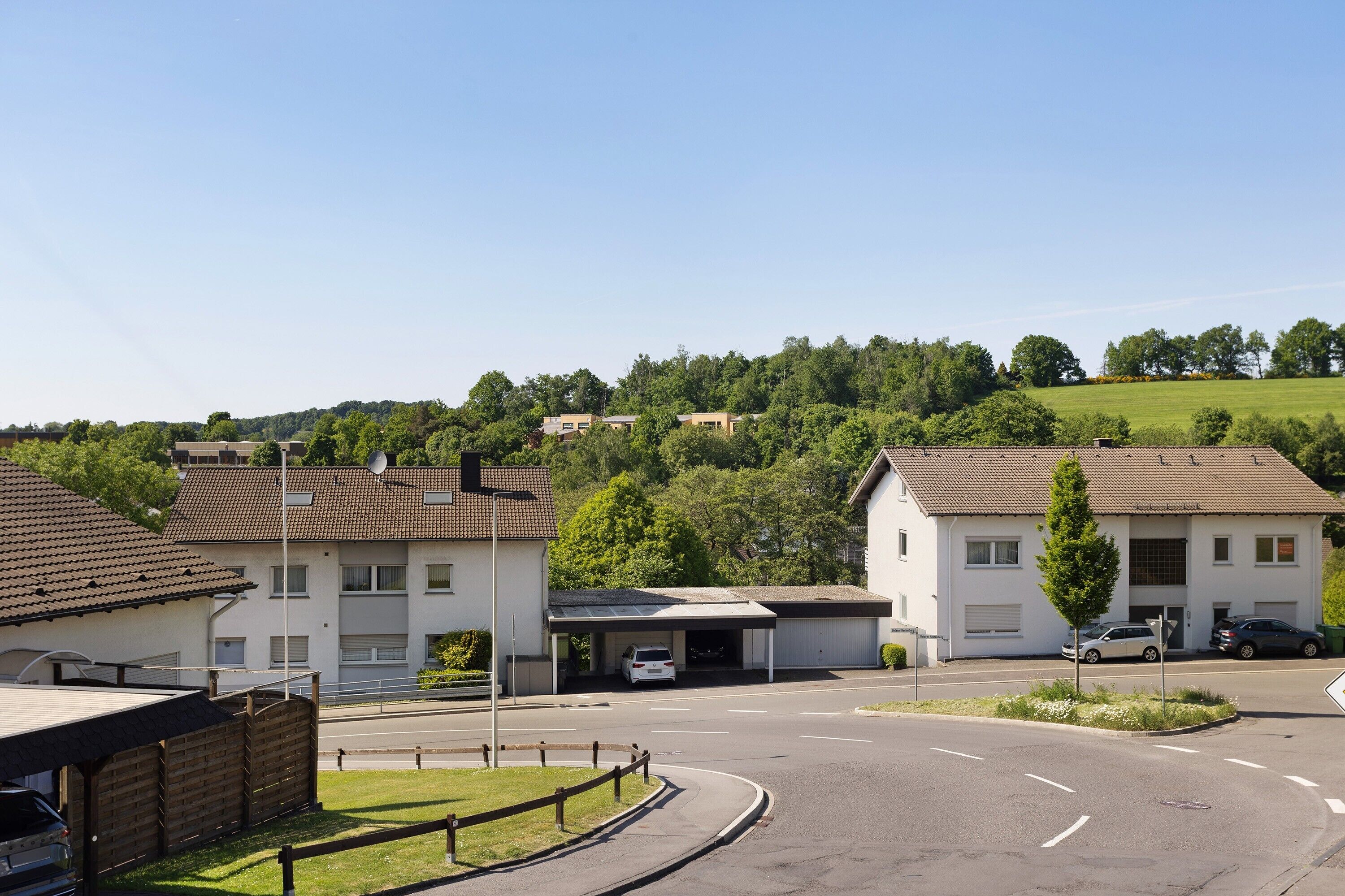 Ein Wohngebiet mit Häusern, einer Straße und einer hügeligen Landschaft im Hintergrund.