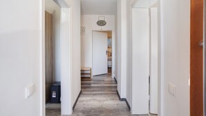 Un pasillo con piso de madera, paredes blancas y una puerta al final.