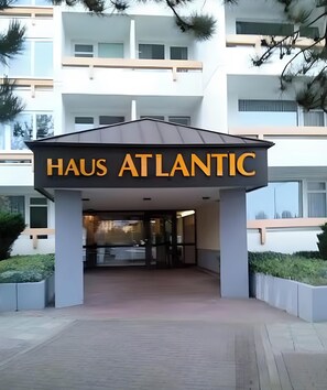 La entrada a un hotel llamado 'HAUS ATLANTIC', con un diseño arquitectónico moderno, que cuenta con un letrero llamativo y una zona de acceso cubierta.