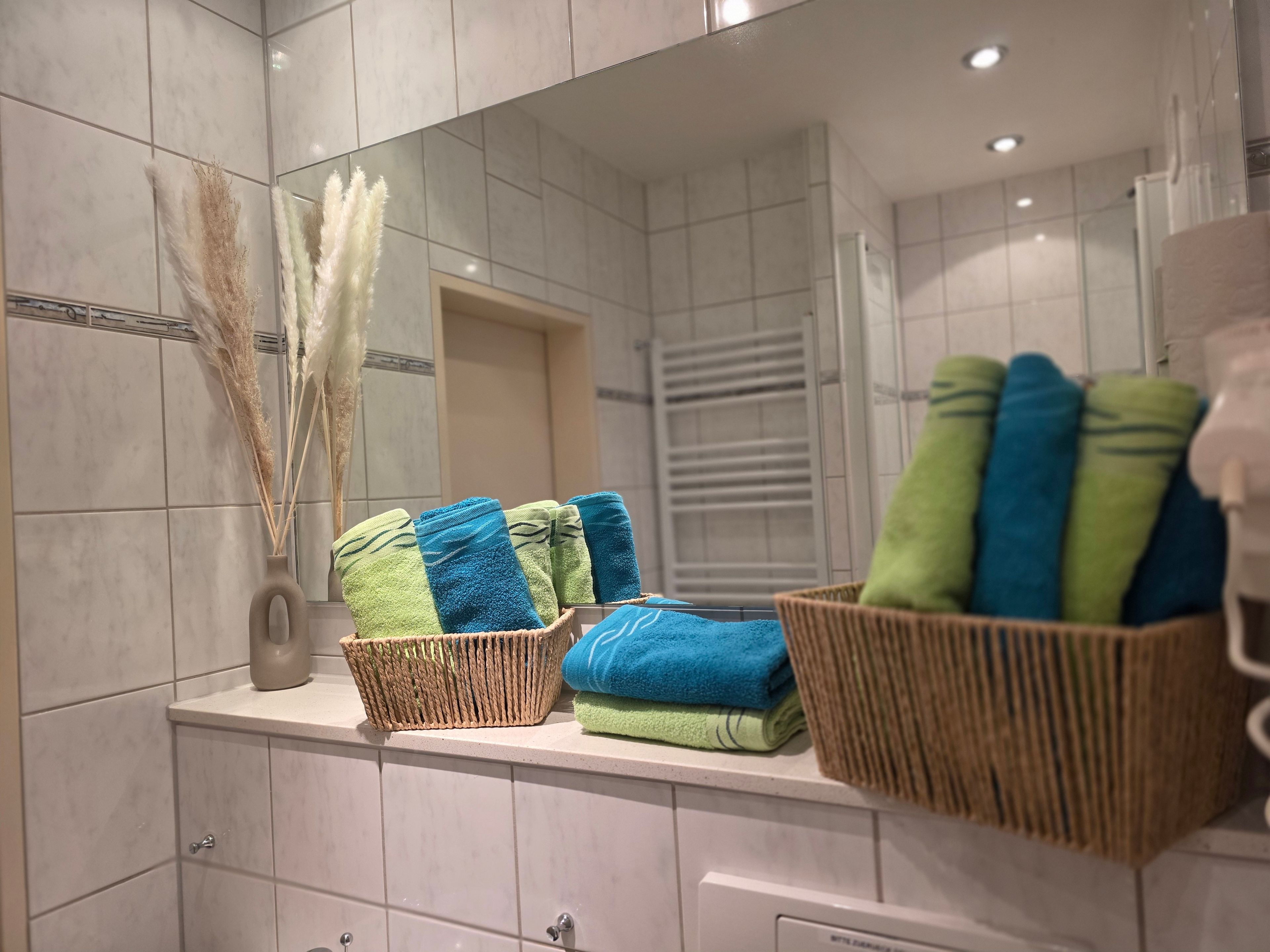 A bathroom with a tiled wall, a mirror, a towel rack with folded towels, and a basket.