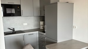 A compact kitchen with grey cabinets, a built-in microwave, a coffee machine, and a small dining table with two chairs. - Apartment 'Dargies' with Sea View, Balcony and Wi-Fi (Cuxhaven)