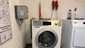 A laundry area with a professional washing machine, a water heater, and a sign indicating new prices for washing and drying. - Apartment 'Dargies' with Sea View, Balcony and Wi-Fi (Cuxhaven)