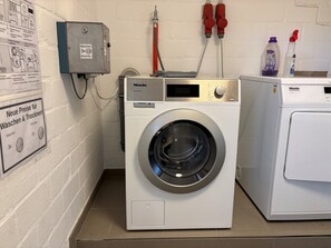 A laundry area with a professional washing machine, a water heater, and a sign indicating new prices for washing and drying. - Apartment 'Dargies' with Sea View, Balcony and Wi-Fi (Cuxhaven)