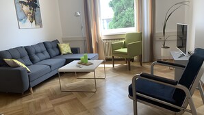 A modern living room with a sofa, a coffee table, a chair, and a TV. - Apartment 'Bodenseeloft HE 66' (Kressbronn am Bodensee)