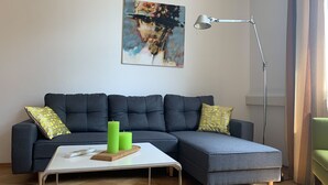 A modern living room with a sectional sofa, a coffee table, a floor lamp, and a painting on the wall. - Apartment 'Bodenseeloft HE 66' (Kressbronn am Bodensee)
