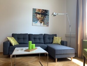 A modern living room with a sectional sofa, a coffee table, a floor lamp, and a painting on the wall. - Apartment 'Bodenseeloft HE 66' (Kressbronn am Bodensee)