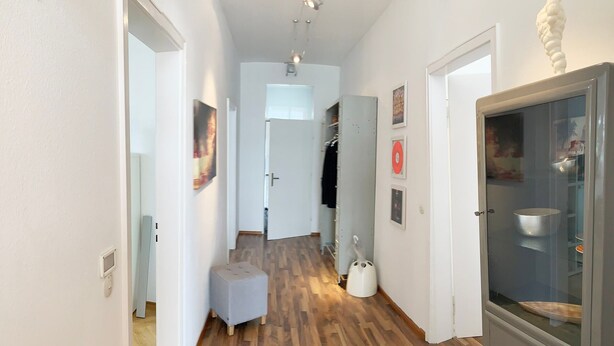 A hallway with wooden flooring, a white door, a small white stool, and a white cabinet with a glass door. - Apartment 'Bodenseeloft HE 66' (Kressbronn am Bodensee)
