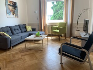 A modern living room with a sofa, a coffee table, a chair, and a TV stand. - Holiday Apartment 'Bodenseeloft H E 66' (Kressbronn am Bodensee)
