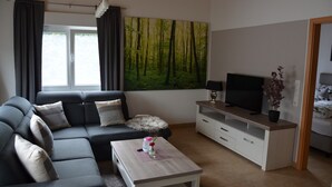 Una sala de estar moderna con un sofá, una mesa de centro, un televisor y un cuadro de un bosque.