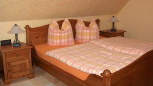 Ein Einzelbett mit Karo-Bettdecke, zwei Nachttische mit Lampen, ein Nachttisch aus Holz mit Lampe und eine Holzkammer mit Schubladen.