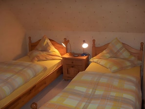 Een slaapkamer met twee eenpersoonsbedden, een nachtkastje met een lamp en een klein ladeblok.