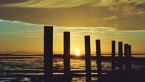 Ein Sonnenuntergang über einem Gewässer mit einer Reihe vertikaler Pfosten im Vordergrund.