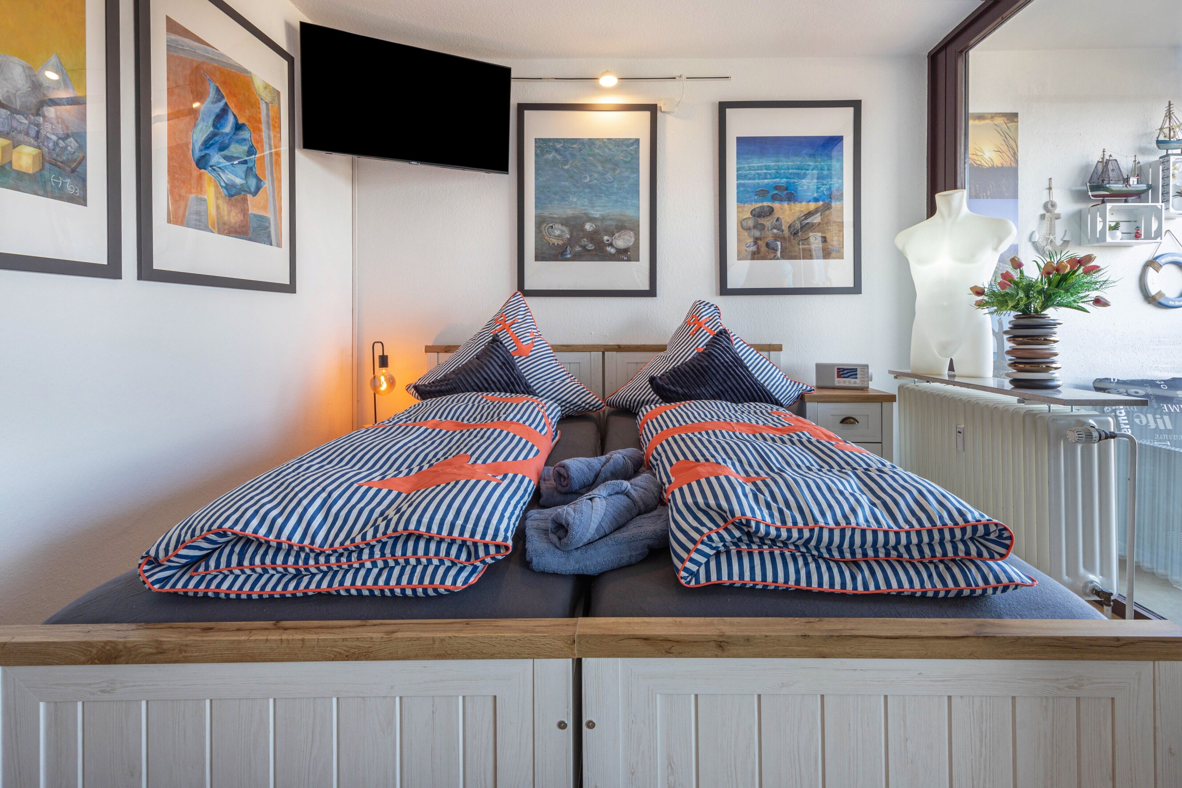 Een kamer met een bed met gestreepte beddengoed, een wandtelevisie, een kunstwerk in een lijst aan de muur, en een raam met uitzicht.