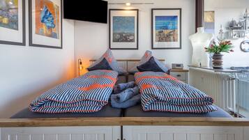 Een kamer met een bed met gestreepte beddengoed, een wandtelevisie, een kunstwerk in een lijst aan de muur, en een raam met uitzicht.