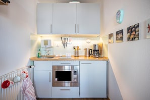 A kitchen with white cabinets, a microwave, a coffee maker, and a clock on the wall.